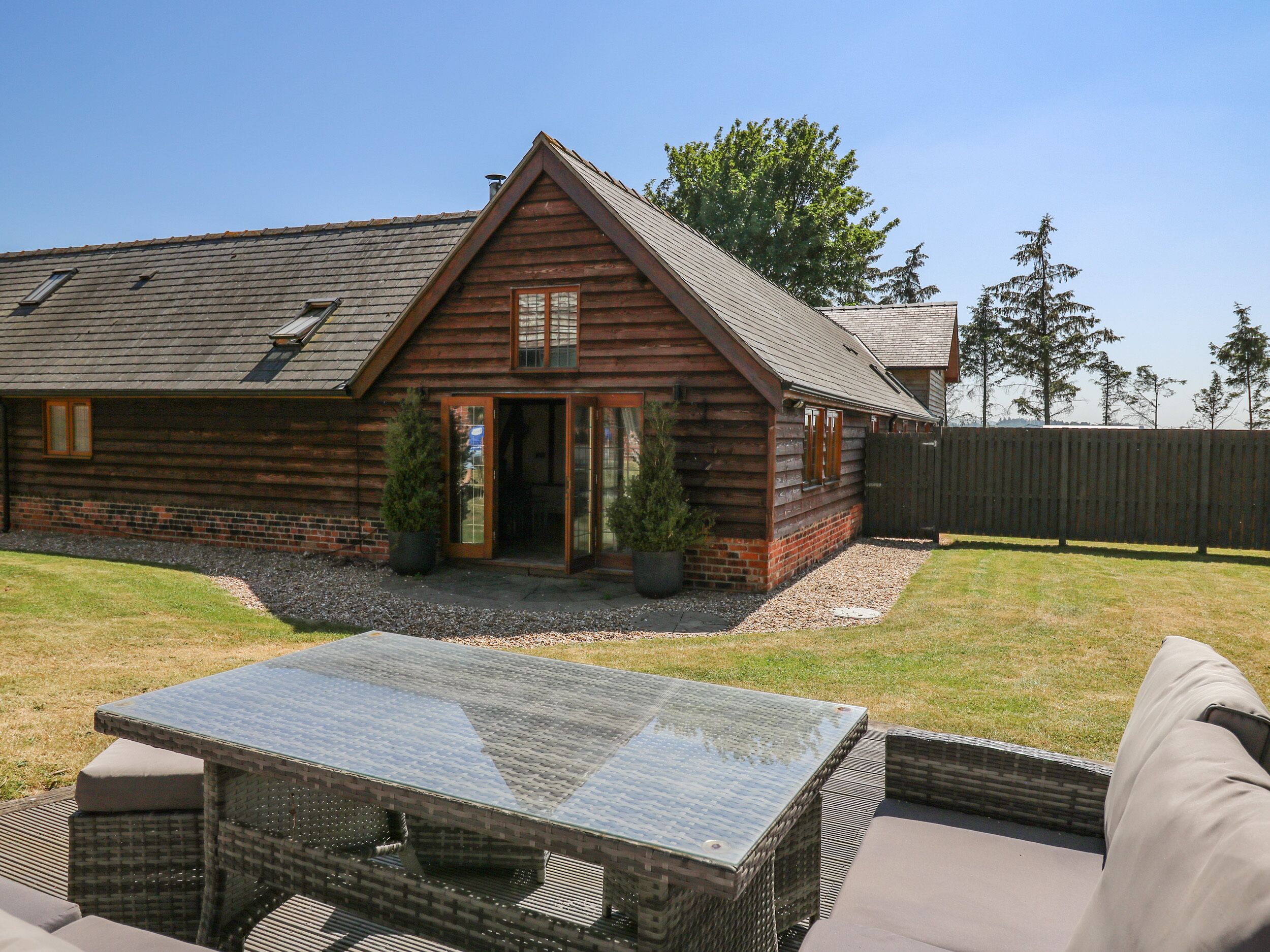 A log cabin with a glass door entrance, a patio with a glass-top table, and a fenced yard.