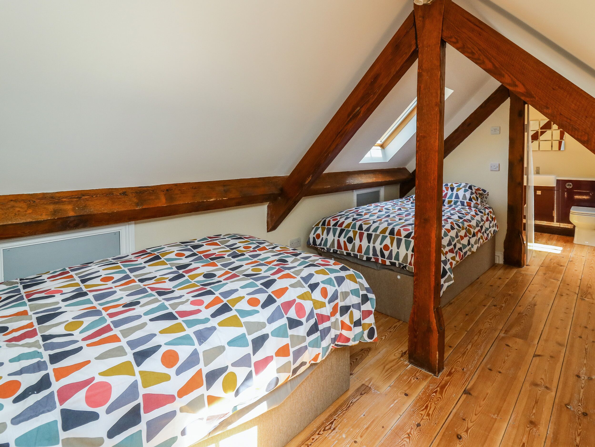 A dormitory room with two beds, wooden beams, a skylight, and a wooden floor.