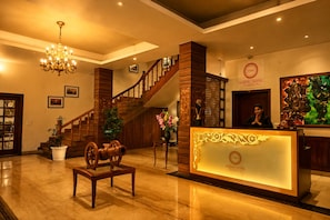 A hotel lobby with a grand staircase, a reception desk, and a chandelier. - Foxoso Misty Oaks Resort (Nainital)