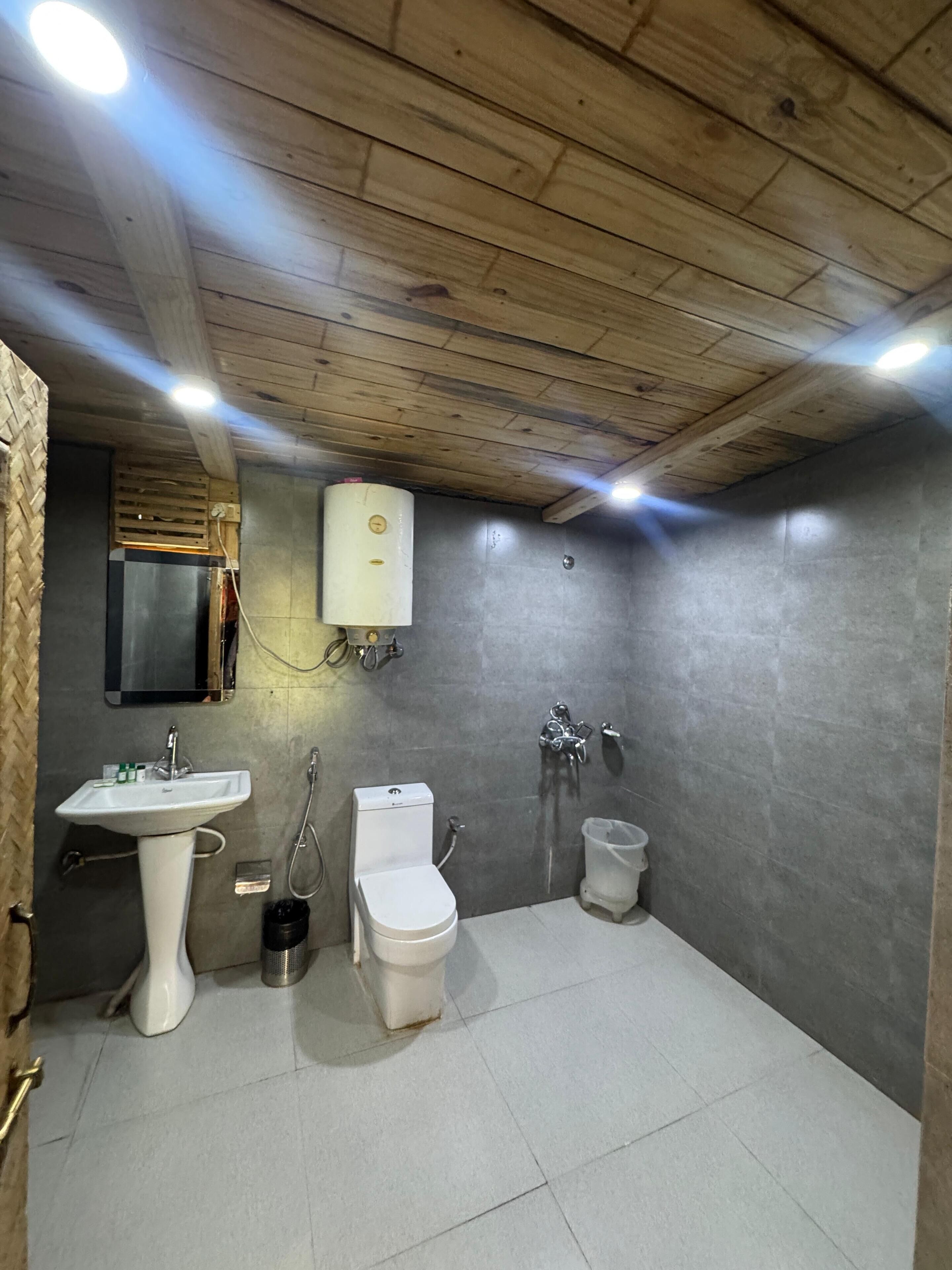 A bathroom with a wooden ceiling, a white sink, a toilet, and a shower.