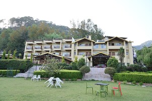 A multi-story hotel with a landscaped garden, outdoor seating, and a view of the surrounding hills.