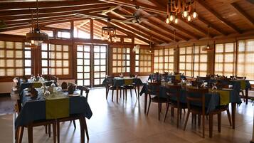 Un vaste espace dédié à la salle à manger, comprenant plusieurs tables, des chaises et des luminaires suspendus.