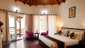 A hotel room with a bed, two chairs, a small table, and a view of the outdoors. - Foxoso Misty Oaks Resort (Nainital)