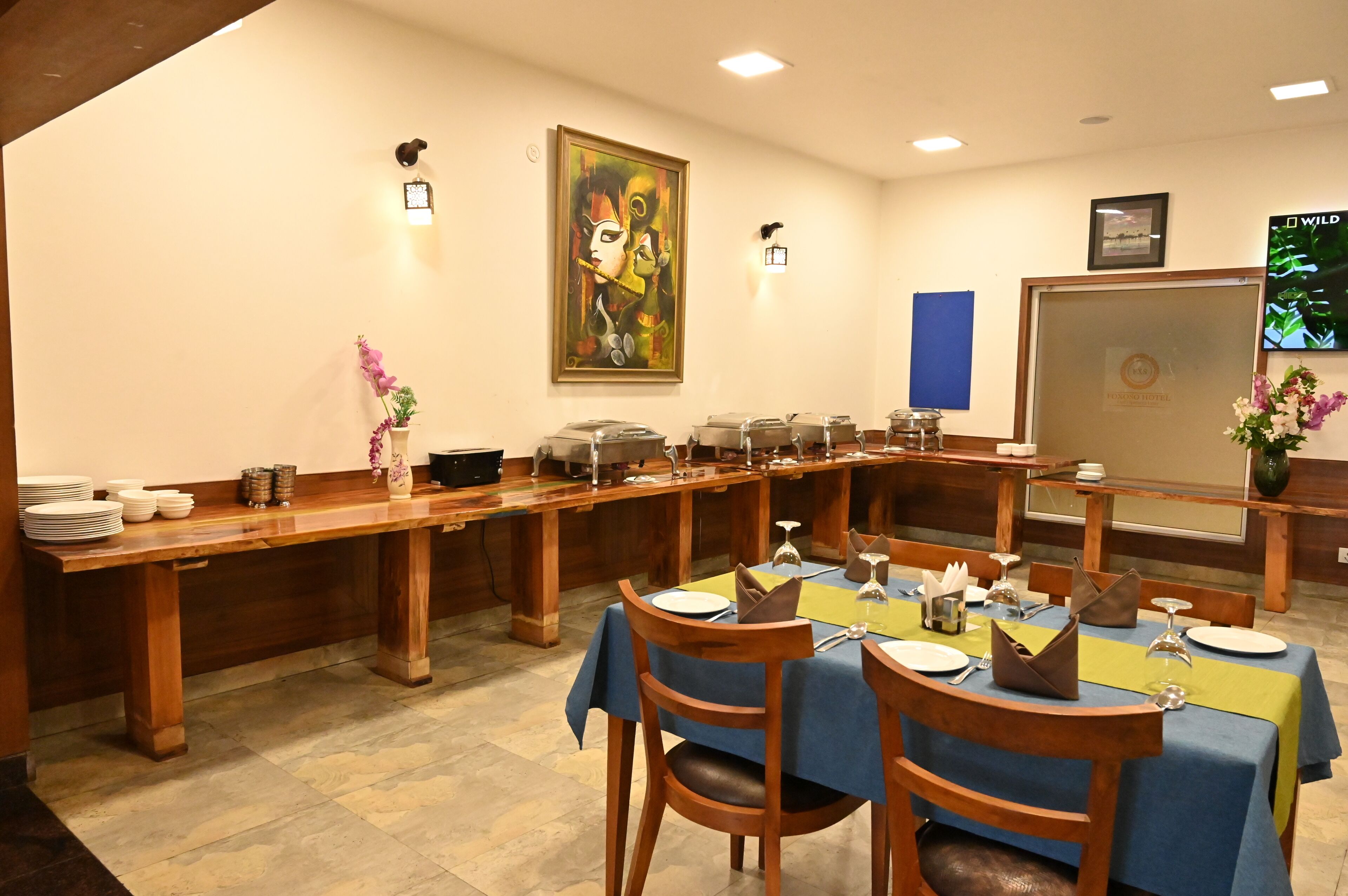 A dining area with a long wooden table set for multiple guests, surrounded by chairs.