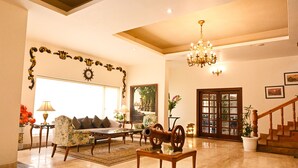 A spacious living room with a large window, a chandelier, and a staircase. - Foxoso Misty Oaks Resort (Nainital)