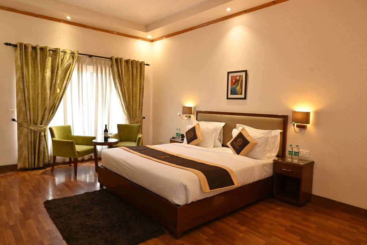 Une chambre d’hôtel avec un grand lit, deux tables de chevet, une petite table d’appoint, une chaise, une petite table et une fenêtre avec des rideaux.