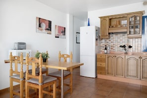 A kitchen with wooden cabinets, a white refrigerator, a dining table with chairs, and a small potted plant.