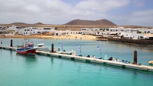 Un pueblo costero con edificios blancos, un muelle con barcos y una montaña al fondo.