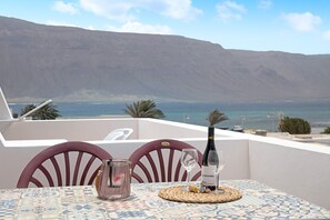 A table with a bottle of wine, a glass, and a candle on a patterned tablecloth, overlooking a body of water and a mountain. - Holiday Home 'Vista Al Mar, La Graciosa' with Sea Views, Private Terrace & Wi-Fi (Caleta de Sebo)