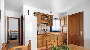 Una cocina con alacenas de madera, un refrigerador, una mesa de comedor con sillas y una planta en maceta.