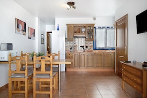 A kitchen with wooden cabinets, a dining table with chairs, a refrigerator, and a TV mounted on the wall.