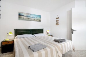 A neatly made bed with striped bedding, two bedside tables with lamps, a wall-mounted picture, and a door with a handle.