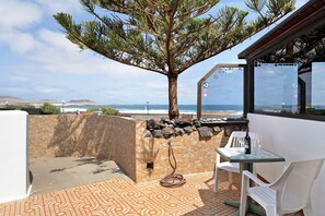 A patio with a stone wall, a tree, a table with chairs, and a view of the sea.