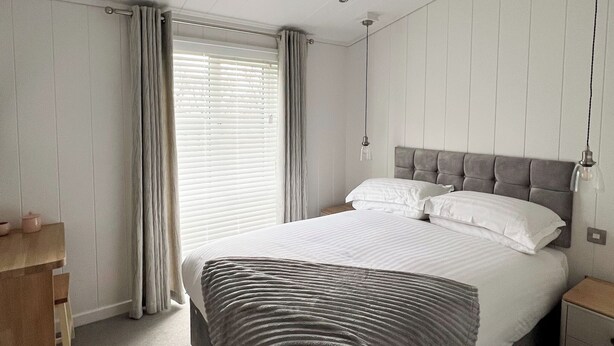 A bedroom with a bed, bedside tables, a desk, and a window with curtains. - Retreat Lodge (3 Bed) (Pooley Bridge, Ullswater)