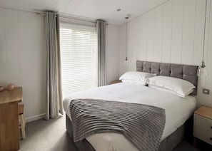 A bedroom with a bed, bedside tables, a desk, and a window with curtains.