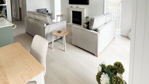 A modern living room with a sofa, a small table, a flat-screen TV mounted above a fireplace, and a dining area with a table and chairs. - Retreat Lodge (3 Bed) (Pooley Bridge, Ullswater)