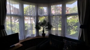 A corner room with large windows, a potted plant, and a sofa. - Ground floor Spacious double bed room, free parking close to seafront. (Bexhill)