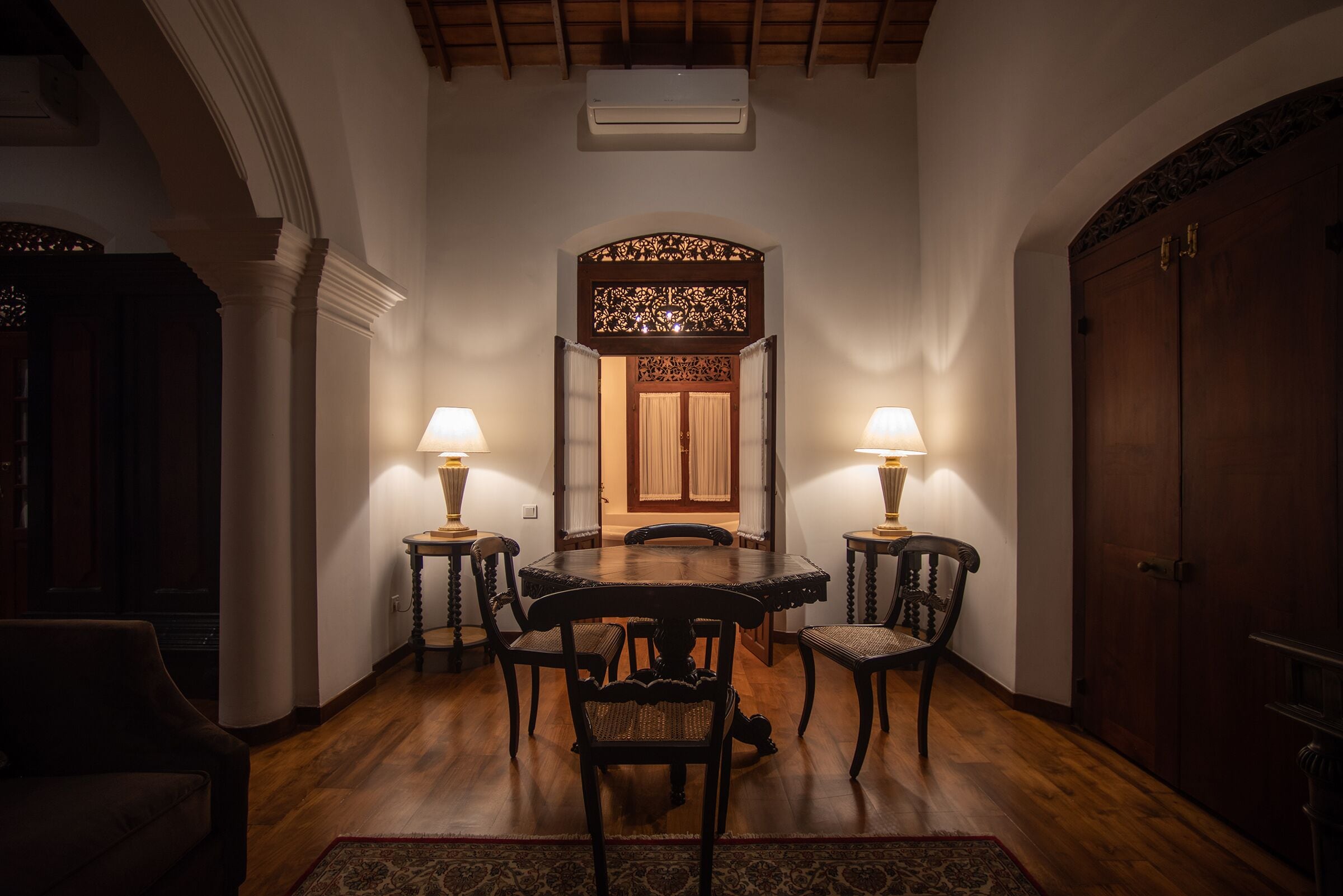 A dining area with a round table, four chairs, two lamps, and a decorative screen.