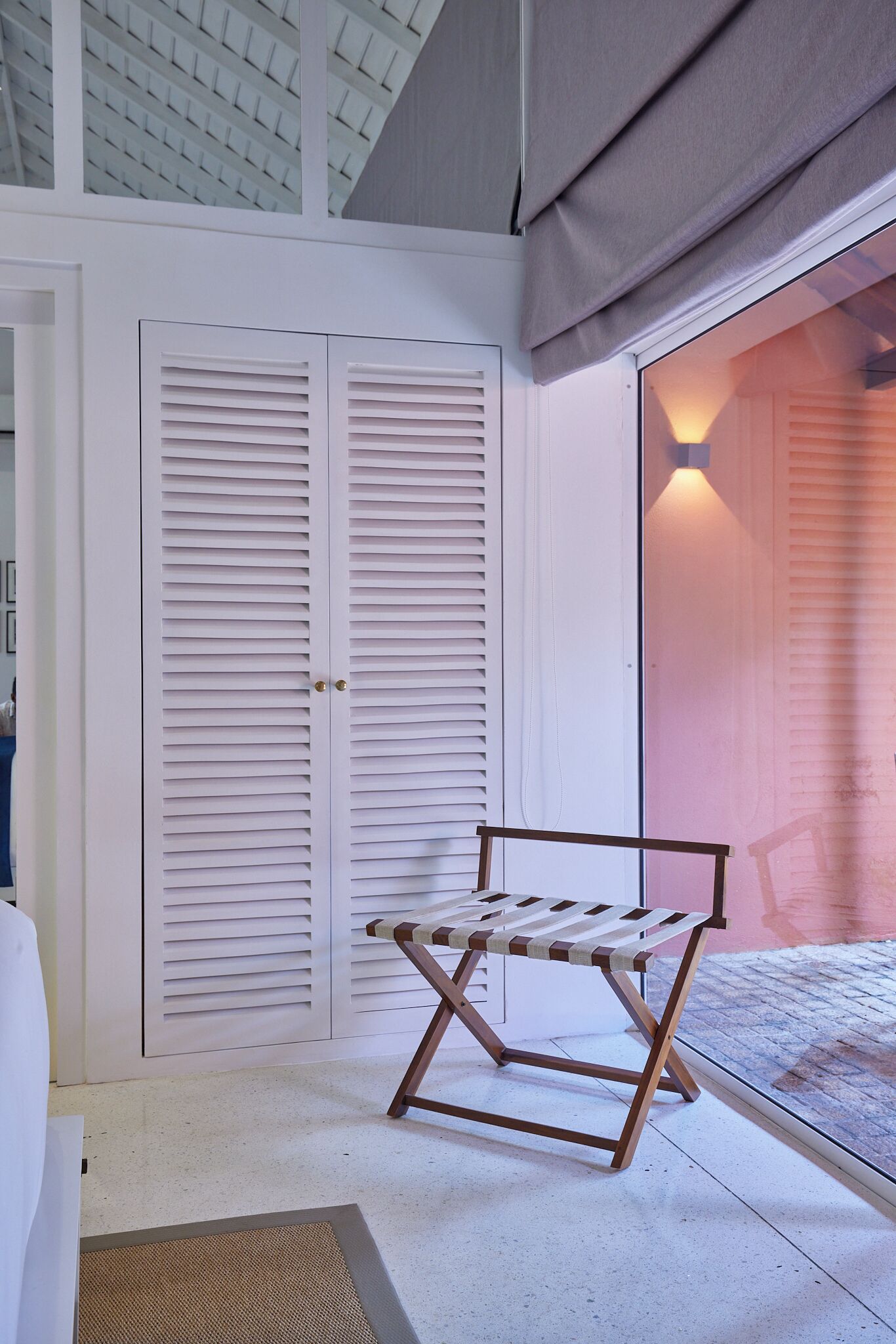 A room with a white wardrobe, a bench, and a window with a view of a building.