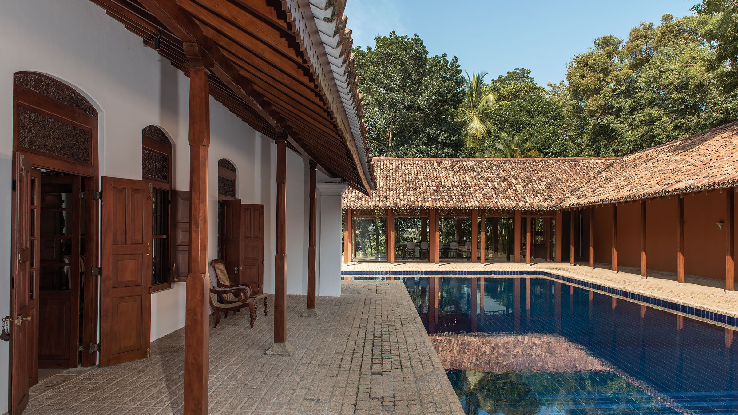 A pool area with a tiled deck, wooden pergola, and a covered seating area.
