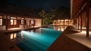 A nighttime swimming pool area with tiled flooring, wooden buildings with large windows, and a clear pool reflecting the lights. - maya tangalle (Tangalle)