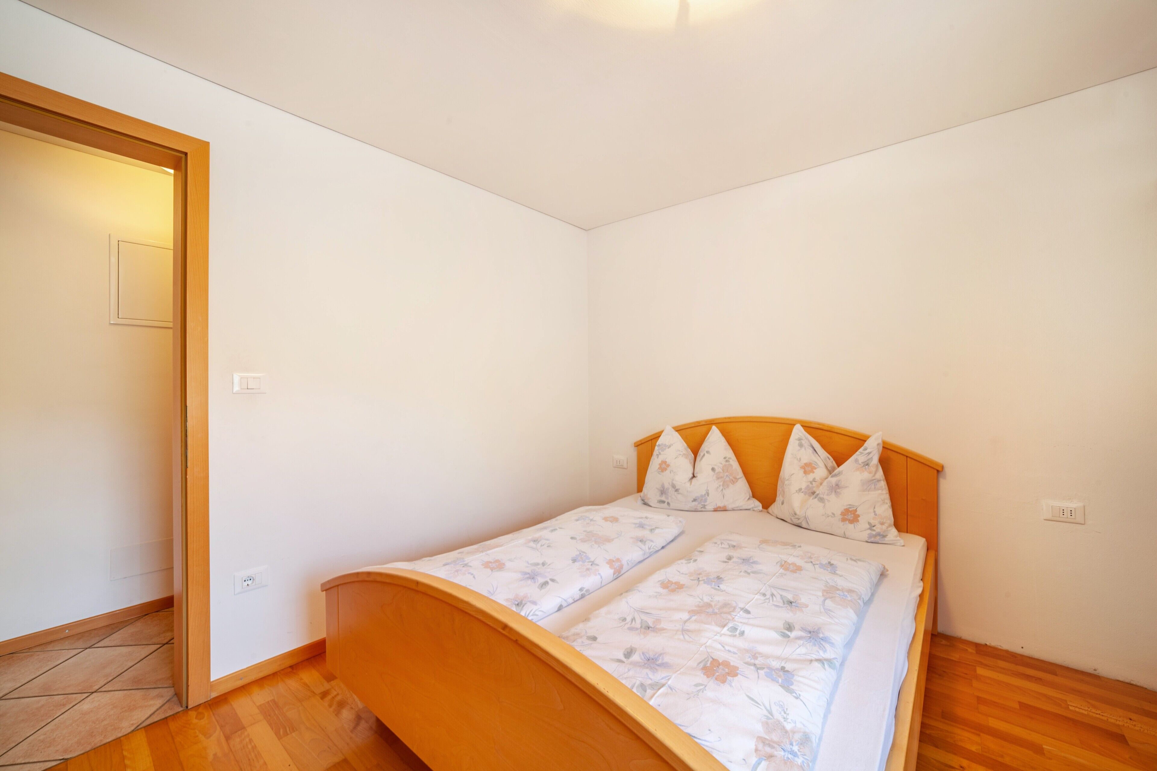 A bedroom with a wooden bed, white walls, and a wooden floor.