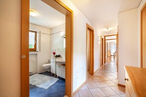 Un couloir menant à une salle de bain équipée de toilettes, d’un lavabo et d’un miroir.