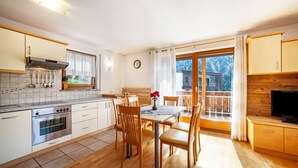 A modern kitchen with a built-in oven, dining table with chairs, and a TV. - Holiday Apartment "Sonnegg" with Mountain View, Balcony & Wi-Fi (Saltaus)