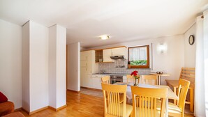 A modern kitchen with white cabinets, a dining area with wooden chairs, and a small table. - Holiday Apartment "Sonnegg" with Mountain View, Balcony & Wi-Fi (Saltaus)