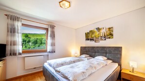 A bedroom with a bed, bedside tables, a window with curtains, a radiator, and wall art. - Holiday Apartment "Sonnegg" with Mountain View, Balcony & Wi-Fi (Saltaus)