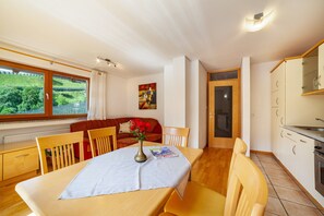 Un comedor con una mesa, sillas, un florero con flores, una revista y vistas al exterior con vegetación.