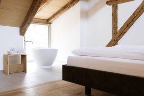Una camera da letto con un letto in legno, una vasca da bagno bianca e una mensola di legno con asciugamani.