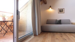 Et værelse med trægulv, en sofa, et bord med stole, en skydedør af glas og en vægmonteret lampe.