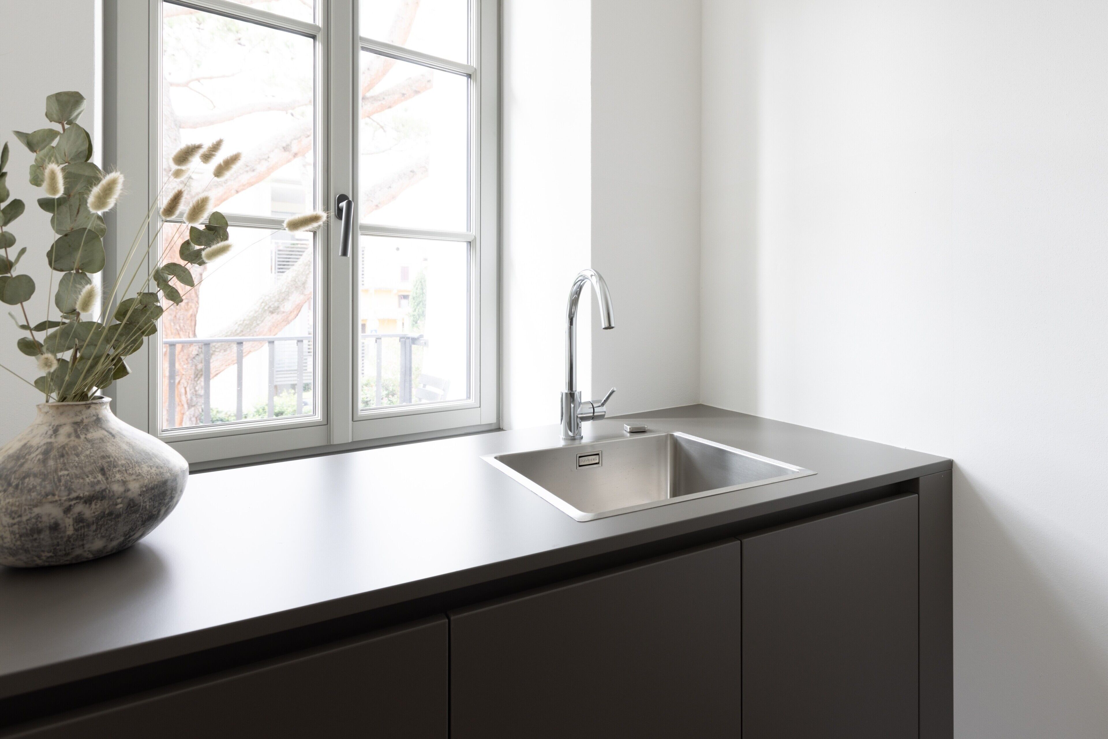 A kitchen with a window, a sink, and a vase with plants.