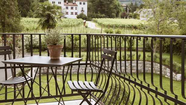 A balcony with a table and chairs, a potted plant, and a view of a building and greenery. - Apartment 'Ansitz Layshof Apt Hauskapelle' with Mountain View, Shared Garden and Wi-Fi (Merano)