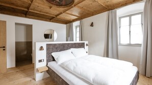 A bedroom with a wooden ceiling, a bed with white bedding, a round mirror, and a window with curtains. - Apartment 'Ansitz Layshof Apt Hauskapelle' with Mountain View, Shared Garden and Wi-Fi (Merano)