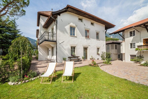 Un bâtiment à deux étages doté d’un balcon, d’un jardin avec un chemin pavé et de deux chaises longues.
