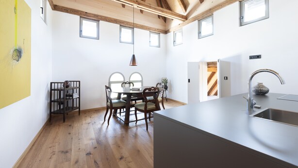 Eine moderne Küche mit Holzbalken, einem Essbereich mit Tisch und Stühlen sowie einer großen Kücheninsel mit Spüle.