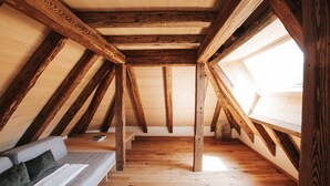 Ein Zimmer mit schrägen Wänden, Holzbalken, einer Couch und einem Oberlicht.