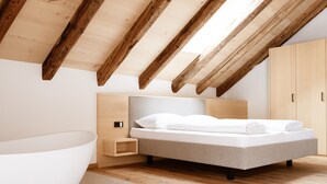 Ein Schlafzimmer mit Schrägdecke, einem Bett, einem Nachttisch, einem Kleiderschrank und einer Badewanne.