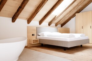 Un dormitorio con techo inclinado, una cama, una mesita de noche, un armario y una bañera.