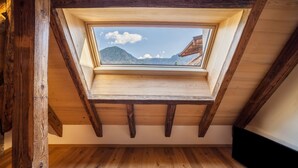 Ein Zimmer mit Dachfenster, Holzbalken und Blick auf Berge.