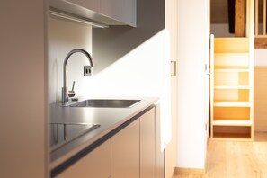 Une cuisine moderne dotée d’un évier en acier inoxydable, d’un four encastré et d’une étagère en bois.
