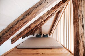 Un dormitorio tipo loft con vigas de madera a la vista, un colchón color beige y suelo de madera.
