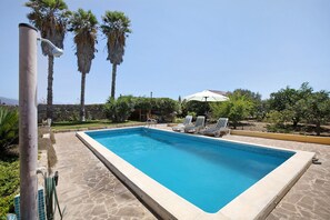 Ein Schwimmbad mit Liegestühlen, einer Pergola und Palmen.