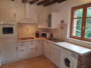 Una cocina con armarios blancos, lavadora, microondas y ventana con vista a vegetación.