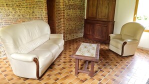 Un soggiorno con parete in mattoni, un mobile in legno, una divano in pelle bianca, una poltrona beige e un tavolino in legno.