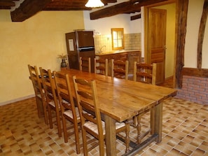 Un coin repas avec une table et des chaises en bois, une cuisine en arrière-plan et un motif de carreaux sur le sol.