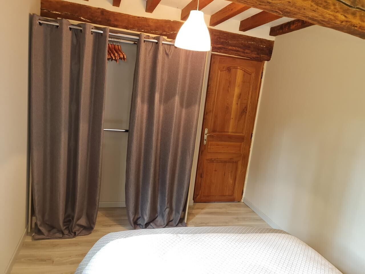 Ein Schlafzimmer mit Bett, Vorhängen, einer Holztür und einer Pendelleuchte.