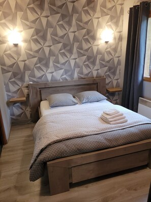 Ein Schlafzimmer mit einer Wand im geometrischen Muster, einem hölzernen Bett mit Kopfteil, zwei Nachttischen und einem Fenster mit Vorhängen.